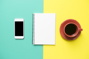 Coffee cup, note book, phone on the yellow and green background