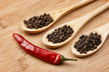 Black and red pepper in wooden spoon on the old board