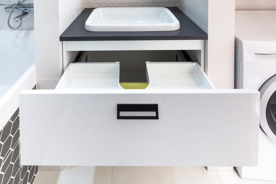 Opened U-shape drawer in a bathroom furniture. White front with black handle, black quartz countertop. 