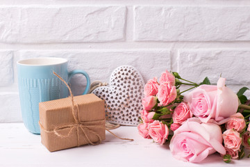Pink roses flowers, decorative heart,  box with present and blue cup on white wooden background.