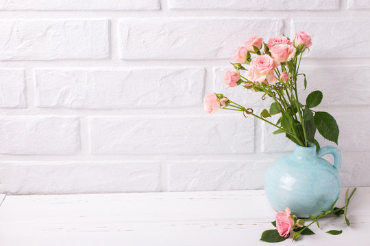 Tender pink roses flowers in blue vase  on  white wooden background near by brick wall.