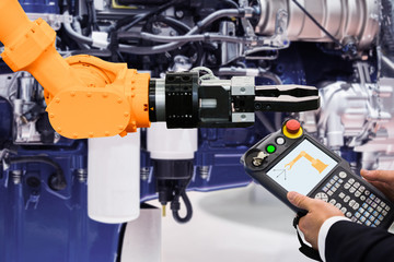 Engineer with teach pendant device. Programming robot with robotic arm at a car service or assembly line