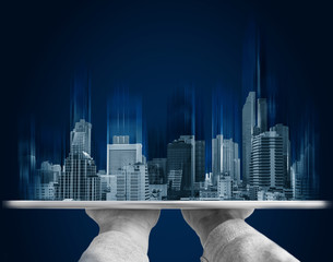 Hand holding digital tablet with futuristic modern buildings hologram, on blue background