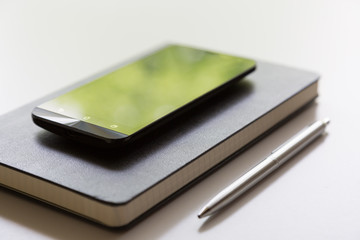 Smartphone sopra agenda e con penna argentata su tavolo bianco