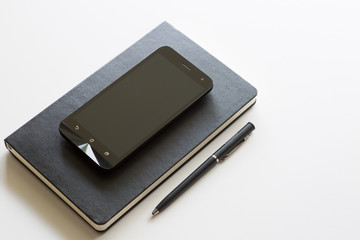 Smartphone sopra agenda e con penna nera su tavolo bianco
