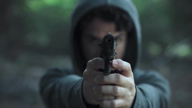 close up portrait of  hooded man pointing the gun at the camera