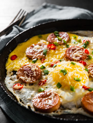 fried eggs with sausage and cheese in a frying pan on wooden table