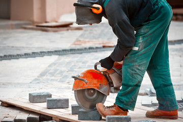 Worker with ear muffs protective equipment cutting the paving slabs with petrol cutting machine at the street. Man protect  hearing from noise hazards on the Job