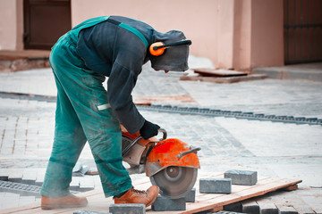 Construction worker cuts walkway slab with circular saw. Man Protect  Hearing From Noise Hazards on...