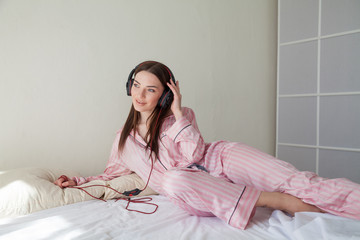 brunette woman in pink Pajamas listening to music with headphones
