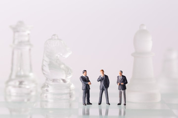 Miniature figurine toys standing on chess board. Focus on the businessman.