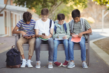 Fototapeta premium School kids using mobile phone and digital tablet on bench