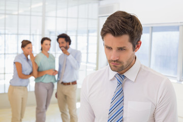 Colleagues gossiping with sad businessman in foreground
