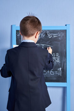 Caucasian schoolboy doing task at a blackboard. Back view.