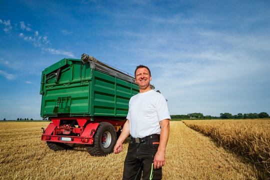 Getreideernte - Landwirt vor Getreideanhänger blickt optimistisch