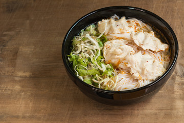 close up of fermented rice noodle with pork soup and vegetable in a ceramic bowl on old wooden table. vietnamese delicious food menu.