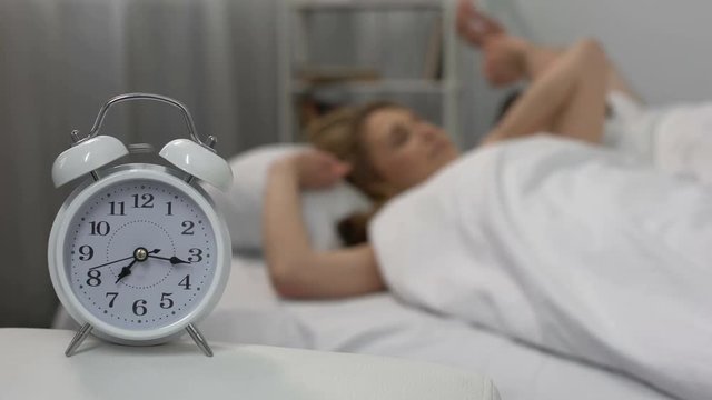 Happy couple waking up with alarm clock in morning and kissing in bed, family