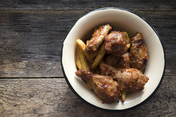 Appetizing chicken pieces and french fries with seasoning in a beautiful old bowl and on an old wooden background and copy space