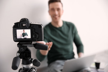 Male blogger with laptop on camera screen near light wall, closeup