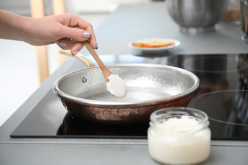 Fototapeta na wymiar Woman putting coconut oil on frying pan in kitchen, closeup