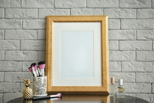 Mockup of blank frame and makeup brushes on table