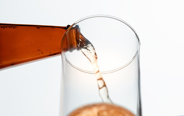 Perk view and close up. Beer poured from a bottle into a glass empty. On white background.