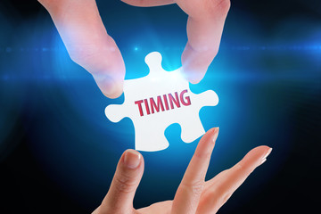 The word timing and hands holding jigsaw against blue background with vignette