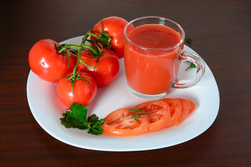 Tomatoes with leaves and tomato juice in the glass mug on white plate