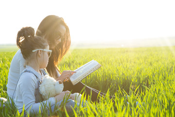 Mom reading a book young daughter in the park