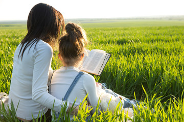 Mom reading a book young daughter in the park