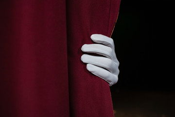 Hand in a white glove pulling curtain away