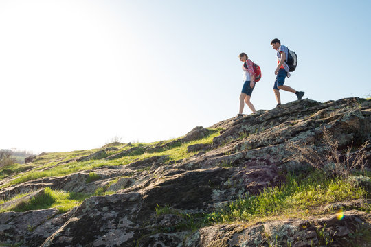 Young Happy Couple Hiking with Backpacks on the Beautiful Rocky Trail at Sunny Evening. Family Travel and Adventure.