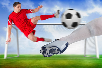 Composite image of football players tackling for the ball with sock and boot against football pitch and goal under blue sky