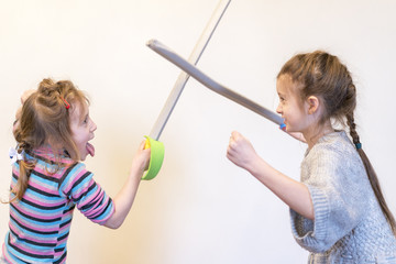 Two girls with toy swords play knights. Children's emotions.