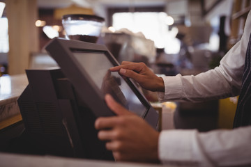 Midsection of waiter touching computer monitor at counter - obrazy, fototapety, plakaty