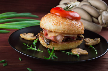 Burger with fried mushrooms, ham, onions and cheese on rustic background