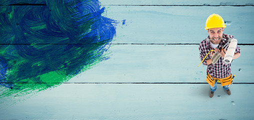 Frustrated handyman holding various tools against painted blue wooden planks