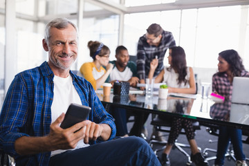 Portrait of happy businessman using mobile phone with team working in background