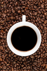 Cup filled with coffee on coffee beans background. Top view.