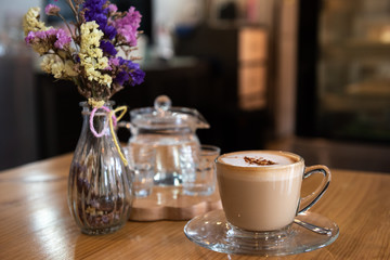 A cup of cappuccino coffee with flowers vase on wooden table