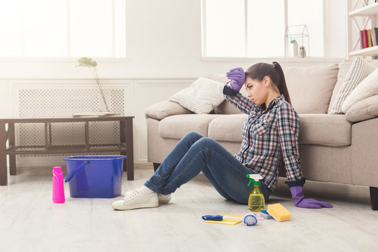 Tired woman cleaning floor with lots of tools