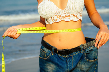 a young and slender girl in denim shorts holds in her hand a measuring yellow tape on her sexy...