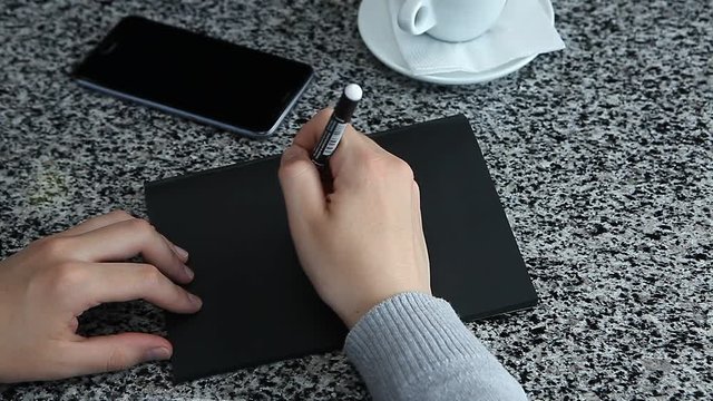 Female hand pretending to write with marker on black craft sketch paper laying table