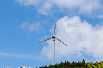 Fototapeta na wymiar Einzelne Windkraftanlage in einem Waldgebiet vor blauem Himmel 