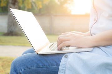 Business asian woman working laptop for socializing on a background blurred in the garden.