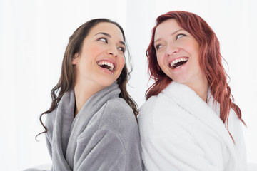Happy female friends in bathrobes standing back-to-back