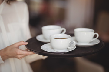 Mid section of waitress holding coffee in tray