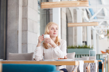 Beautiful successful young businesswoman sits at the table of a street cafe and drinks coffee in good mood in the morning