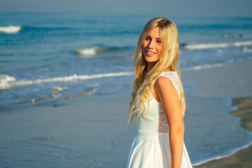 Fototapeta na wymiar young and beautiful bride with long blond hair beautifully smiling and walking on the sea in beautiful white long wedding dress. a happy bride married a wedding ceremony on the beach by the sea