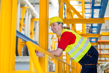 Happy worker in yellow reflective suit with yellow helmet relaxing in a factory and smiling. Worker in a factory smiling